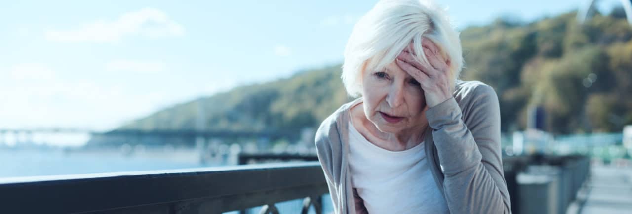An older person on a boardwalk, holding their head in distress