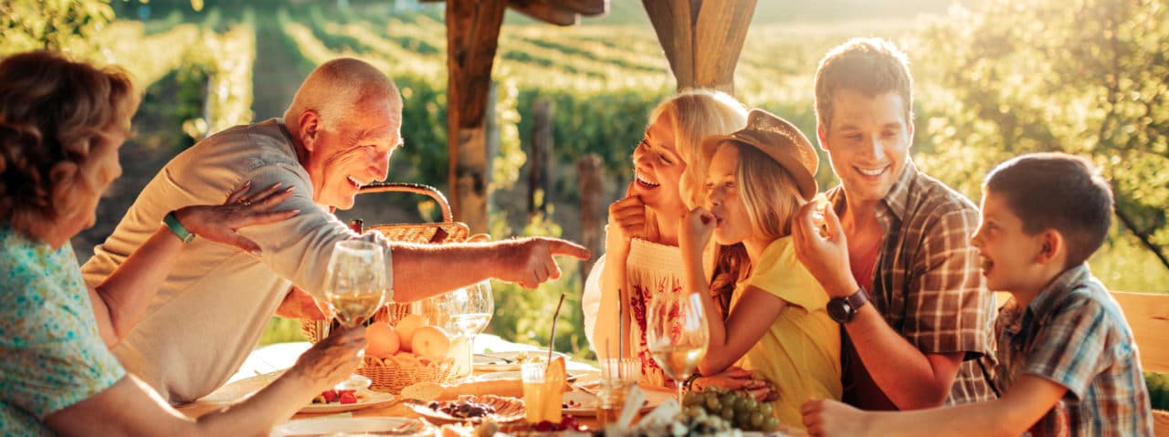 Multiple generations gathered around an outdoor meal table, all laughing and smiling