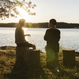 Two people speaking outside near a lake.