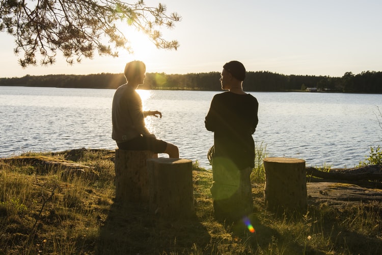 Two people speaking outside near a lake.