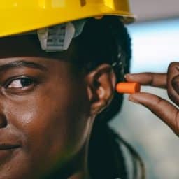 Female construction working putting in earplugs to protect her hearing.