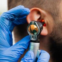 Man gets an ear exam. Doctor's hand in blue glove with otoscope.