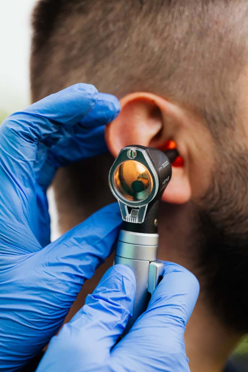 Man gets an ear exam. Doctor's hand in blue glove with otoscope.
