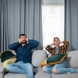 Two people on the couch covering their ears to block out noise