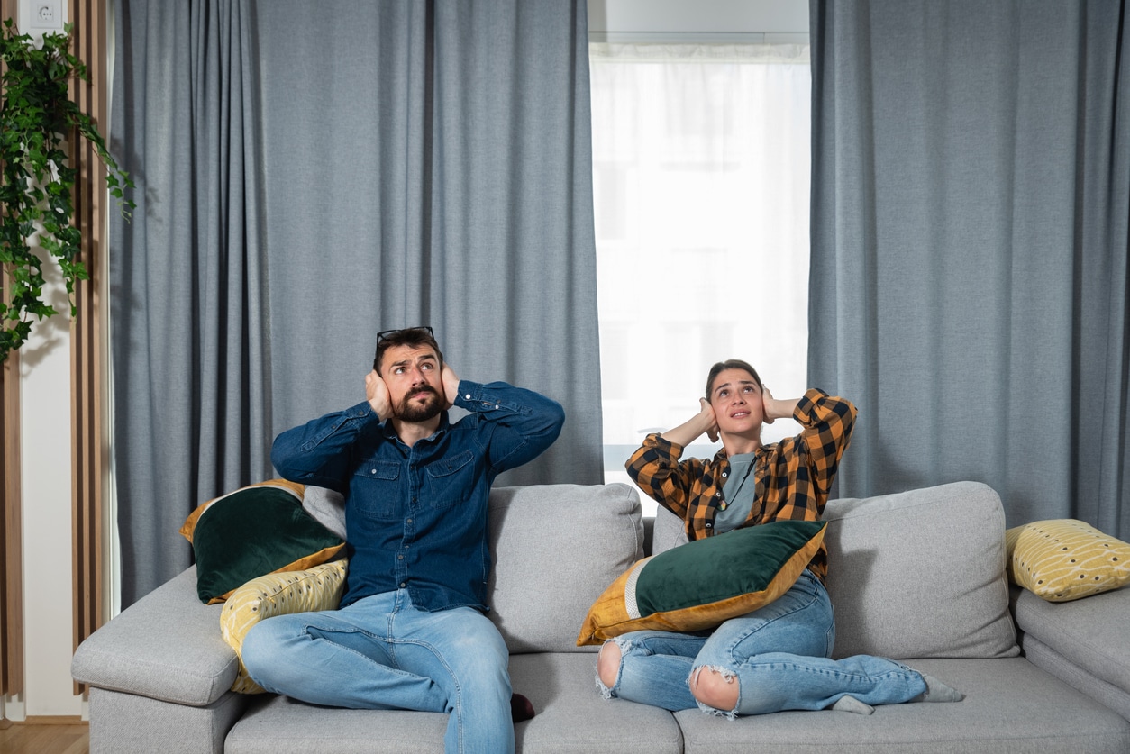 Two people on the couch covering their ears to block out noise.