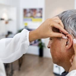 Doctor adjusts hearing aid behind man's ear