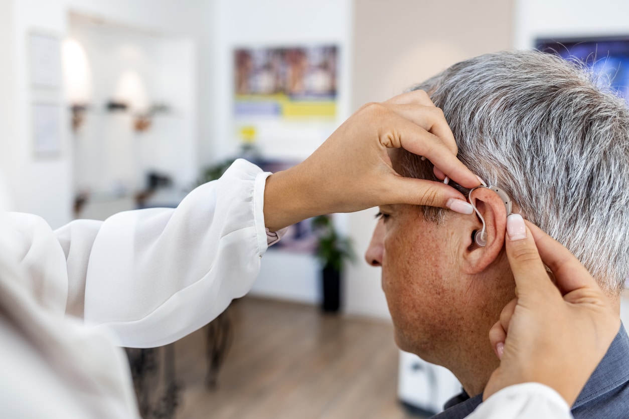 Doctor adjusts hearing aid behind man's ear