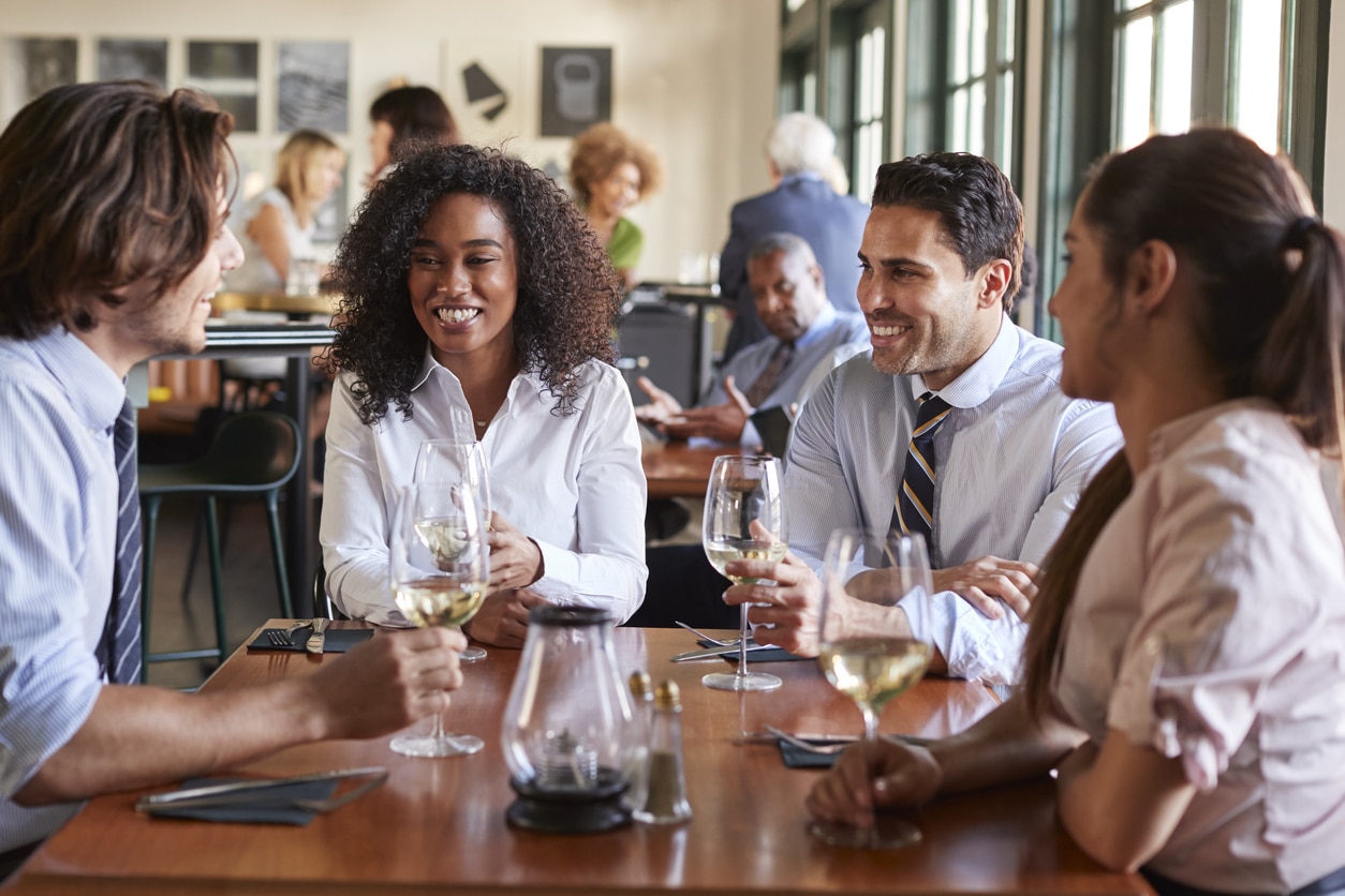 Four friends drinking wine in a busy restaurant.